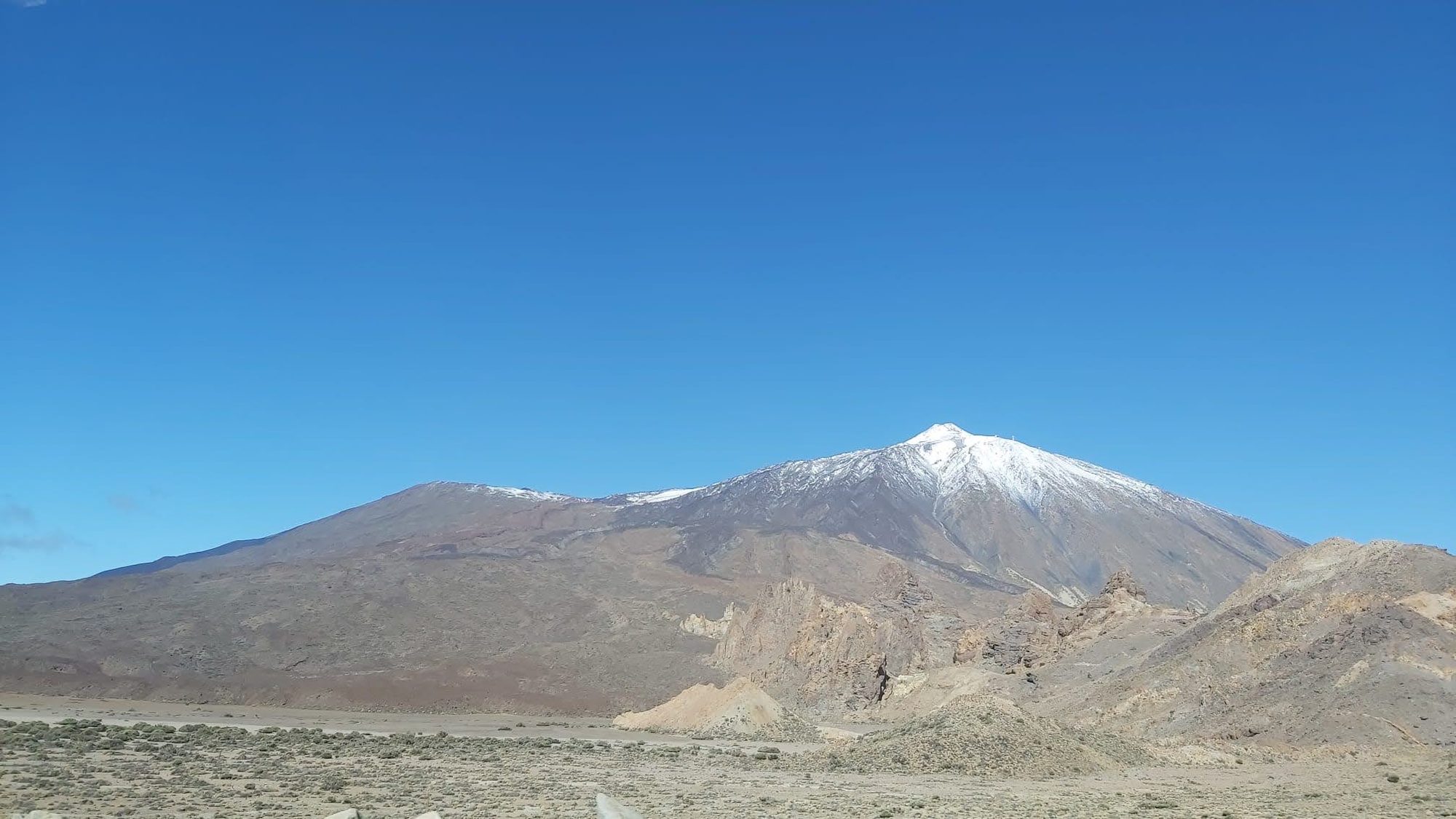 Vista del volcán Teide nevado sobre el paisaje árido bajo un cielo azul despejado.